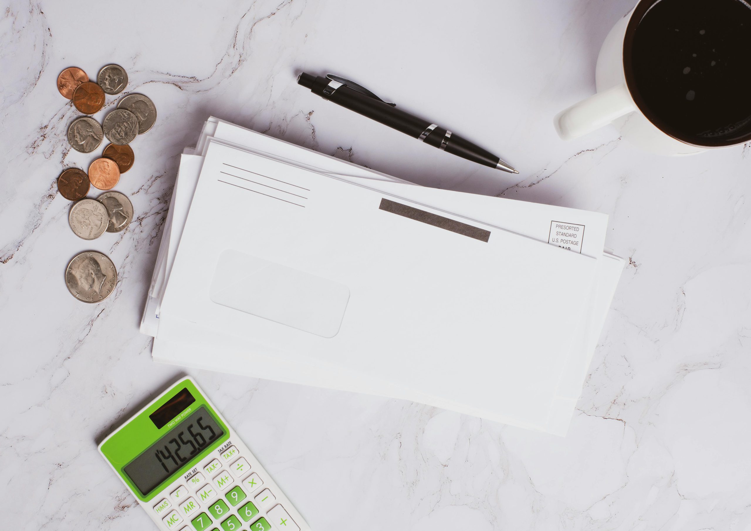 Flat lay of financial documents, calculator, coins, and coffee cup on marble surface.